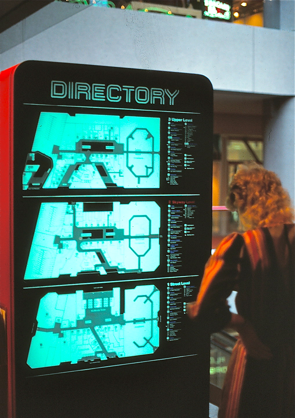 Woman looking at a raised three level directory by an escalator.