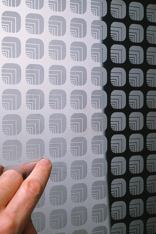 Closeup of an elevator door with a hand pointing to the repeat pattern of Oxford logos.